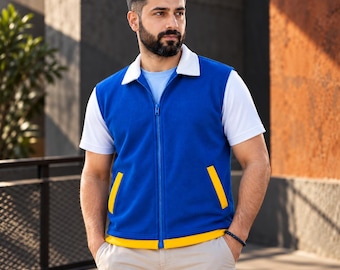 以下が含まれることがあります： 白い襟とポケットおよび裾に黄色のトリムが付いた青いノースリーブのジップアップベスト。白い半袖シャツと明るい色のパンツの上に着用されています。ベストにはフルレングスの青いジッパーと、黄色のアクセントが付いた2つのポケットがあります。