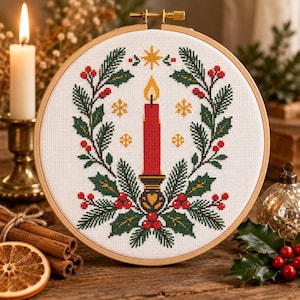 May include: A circular wooden embroidery hoop containing a cross-stitch design on white fabric. The pattern features a central red candle in a holder, surrounded by a wreath of green pine branches, red berries, and small gold star accents.
