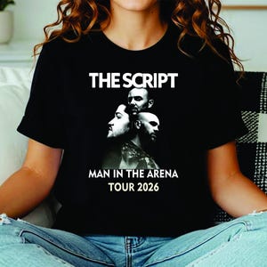 May include: A black short-sleeved t-shirt featuring a white graphic print of the band The Script. The design includes the text THE SCRIPT at the top and MAN IN THE ARENA TOUR 2026 at the bottom, surrounding a black and white portrait of three band members.