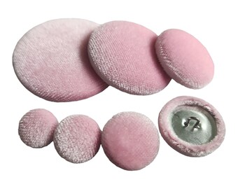 May include: A set of pink velvet buttons in various sizes. The buttons are soft and have a subtle sheen. Some buttons have a metal shank for sewing.