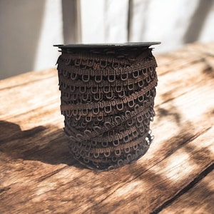 May include: A roll of brown elastic trim with a series of small loops. The trim is wound around a black plastic spool.