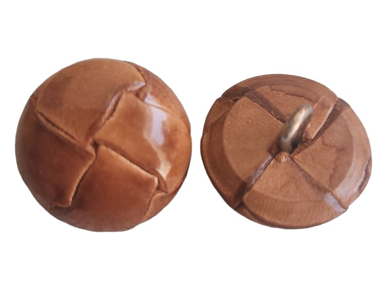 May include: Two brown leather buttons with a stitched design. One button is round and the other is flat with a shank.