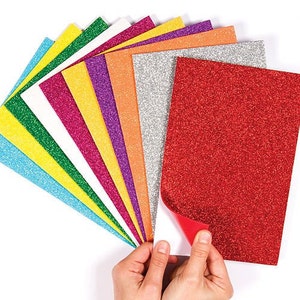 May include: A collection of glitter paper sheets in various colors, including red, silver, orange, purple, pink, white, green, yellow, and blue. The red sheet is being peeled back to reveal a white backing.