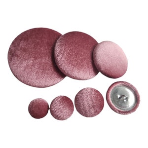May include: A set of seven pink velvet buttons in various sizes. The buttons are round and have a smooth, soft texture.
