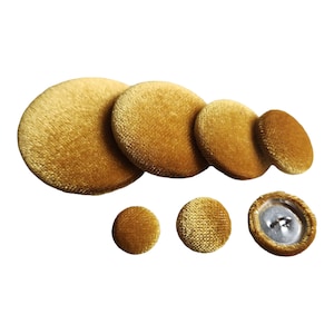 May include: Assortment of six gold velvet buttons in various sizes. The buttons have a smooth, soft texture and a classic round shape.