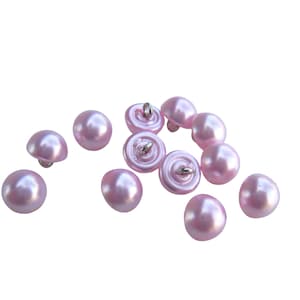 May include: A group of 10 pink plastic buttons with a shiny finish. The buttons are round and have a flat back. Some of the buttons have a metal shank.