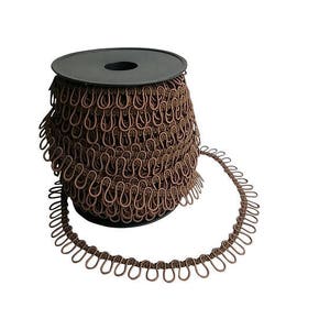 Peut inclure: Une bobine de galon élastique brun avec des boucles métalliques. Le galon est enroulé autour d'une bobine en plastique noir.
