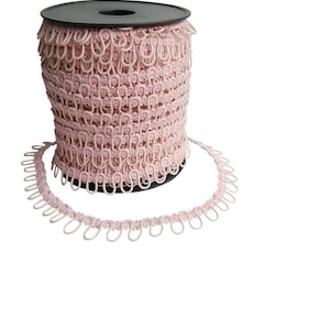 May include: A spool of pink elastic trim with small loops. The trim is wound around a black plastic spool.