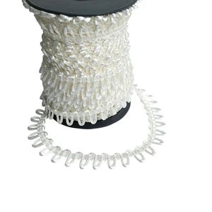 May include: A roll of white decorative trim with a looped edge. The trim is wound around a black plastic core. The looped edge creates a textured, fringed appearance. Suitable for sewing, crafting, and embellishments.