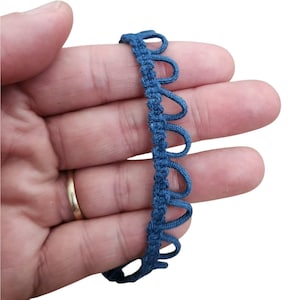 May include: A length of blue decorative trim with a scalloped edge. The trim is a solid blue colour and has a looped design along one edge. The trim is held in a hand.
