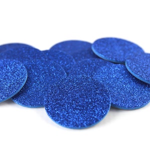 May include: A collection of blue glittery, oval-shaped embellishments. The embellishments are scattered across a white background. The glitter adds a sparkling effect to the objects. These could be used for crafts or decorations.