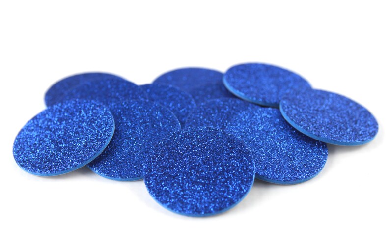May include: A collection of blue glittery, oval-shaped embellishments. The embellishments are scattered across a white background. The glitter adds a sparkling effect to the objects. These could be used for crafts or decorations.