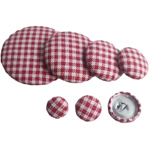 May include: Set of red and white gingham fabric buttons in various sizes. The buttons are round and have a smooth surface.
