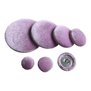 May include: A set of six purple velvet buttons in various sizes. The buttons are round and have a smooth, velvety texture. One button has a silver shank.