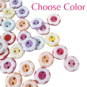 May include: A collection of flower-shaped buttons in various pastel colors, including pink, yellow, purple, and blue. Each button has a contrasting center and two holes for sewing. The text "Choose Color" is displayed in pink.