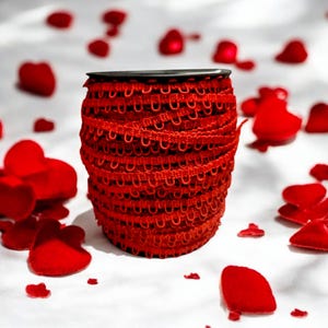 May include: A spool of red elastic trim with a scalloped edge. The trim is surrounded by red felt hearts.