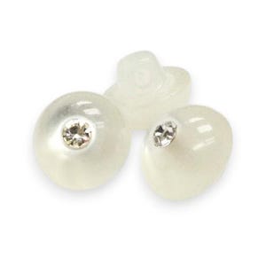 Puede incluir: Tres botones nacarados blanquecinos con una gema clara y facetada en el centro de cada uno. Un botón es un disco plano, mientras que los otros dos son redondeados. También se ve un cuarto botón translúcido.