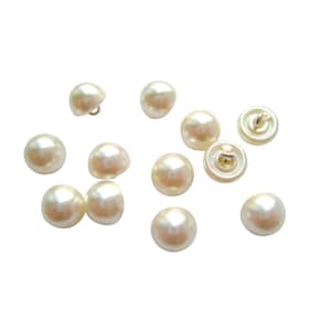 May include: A collection of twelve white pearl-like buttons with a gold metal shank on the back.