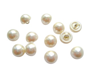 May include: A collection of twelve white pearl-like buttons with a gold metal shank on the back.