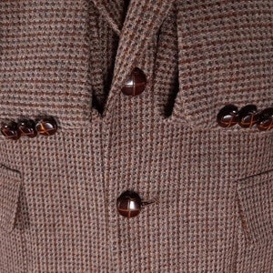 May include: A brown tweed blazer with four brown buttons. The blazer has a pocket on the left side.