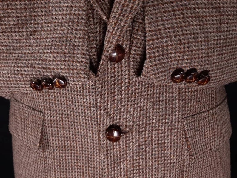 May include: A brown tweed blazer with four brown buttons. The blazer has a pocket on the left side.