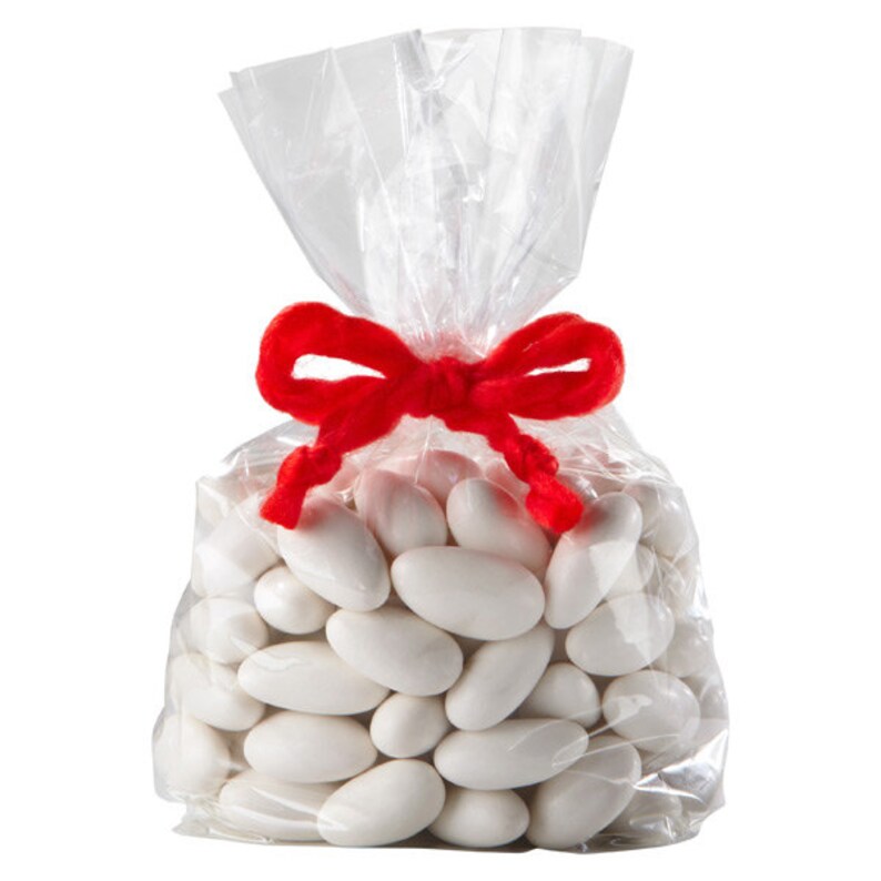 Op de afbeelding: Een doorzichtige plastic zak gevuld met witte amandelvormige snoepjes, vastgebonden met een rood lint.