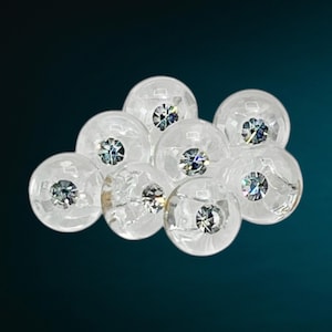 May include: A cluster of eight clear glass beads with iridescent rhinestones inside. The beads are arranged in a loose, cloud-like formation.