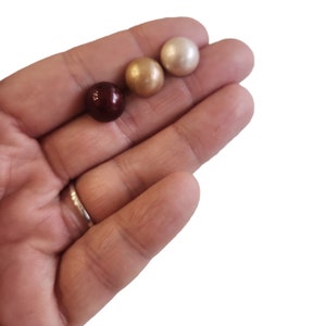 May include: Three round pearl beads in different colors: brown, gold, and white.
