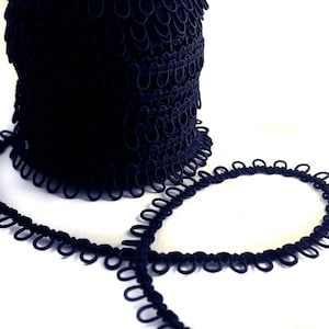 May include: A roll of black elastic trim with small loops. The trim is coiled and a section is unrolled to show the detail.