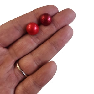 May include: Two red metallic spheres, one slightly larger than the other, are held in a person's hand.