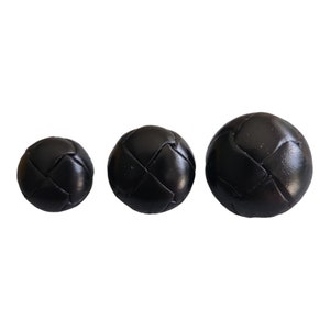 May include: Three black leather buttons with a woven design. The buttons are different sizes.