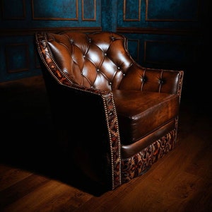 May include: A brown leather armchair with a tufted back and seat. The chair has a decorative patterned trim around the edges and is sitting on a wooden floor.