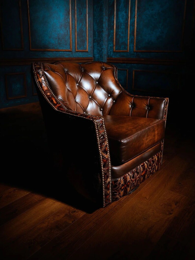 May include: A brown leather armchair with a tufted back and seat. The chair has a decorative patterned trim around the edges and is sitting on a wooden floor.