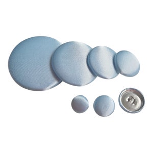 May include: A set of six light blue fabric covered buttons in various sizes. The buttons are round and have a smooth, satin-like finish.