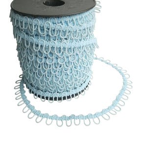 May include: A spool of light blue curtain tape with metal rings. The tape is wound around a black plastic spool.