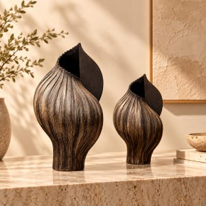 Puede incluir: Dos jarrones decorativos con una forma orgánica similar a una concha. Los jarrones presentan una superficie texturizada y acanalada con un acabado en bronce oscuro y negro. Cada pieza tiene una abertura ancha y curva que se estrecha hacia la base.
