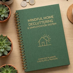 Pode incluir: Uma agenda de espiral com capa de tecido verde-escuro com texto dourado que diz MINDFUL HOME DECLUTTERING & SIMPLIFICATION SYSTEM, um ícone de casa em linhas com um sol e o texto COMPLETE PLANNER, CHECKLISTS & TRACKERS.