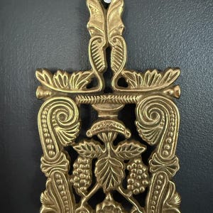 Salvamanteles antiguo de latón macizo con asa y diseño floral calado de vid.