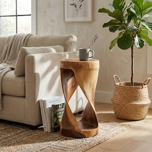 May include: A cylindrical wooden side table featuring a natural grain finish and a central twisted hourglass-shaped cutout. The table has a smooth, flat circular top surface and a solid base, showcasing the organic texture and warm brown tones of wood.