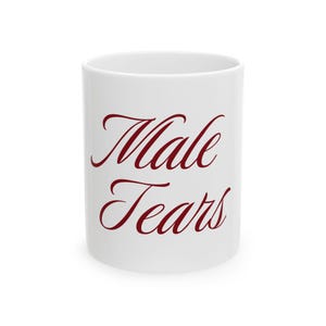 Puede incluir: Una taza de cerámica blanca con el texto "Male Tears" impreso en una fuente cursiva de color rojo oscuro. La taza tiene una forma cilíndrica con un acabado liso y brillante que resalta las letras de color rojo oscuro en el centro.