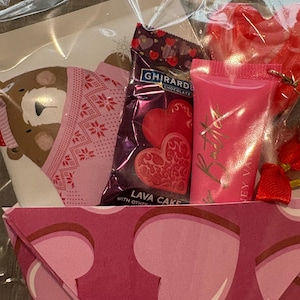 Puede incluir: Una cesta de regalo de San Valent&iacute;n envuelta en celof&aacute;n transparente. La cesta contiene una barra de chocolate Ghirardelli, caramelos en forma de coraz&oacute;n, un tubo de brillo labial rosa y una tarjeta decorativa.
