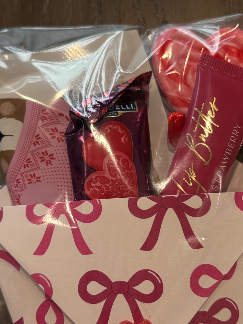 Puede incluir: Una cesta de regalo con tem&aacute;tica de San Valent&iacute;n. Contiene caramelos en forma de coraz&oacute;n, un tubo de manteca labial de fresa y una mascarilla facial con estampado rosa. La cesta est&aacute; decorada con lazos rosas.