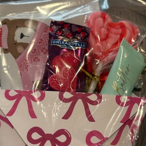 Puede incluir: Un juego de regalo en una bolsa de celof&aacute;n transparente, que contiene una tarjeta rosa y blanca con tem&aacute;tica de oso, un cuadrado de chocolate Ghirardelli, una piruleta en forma de coraz&oacute;n y un tubo de loci&oacute;n de mantequilla. La tarjeta est&aacute; decorada con lazos rosas.