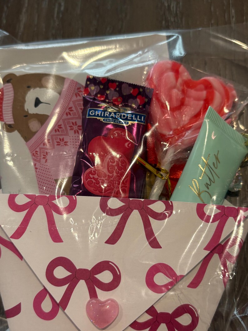 Puede incluir: Un juego de regalo en una bolsa de celof&aacute;n transparente, que contiene una tarjeta rosa y blanca con tem&aacute;tica de oso, un cuadrado de chocolate Ghirardelli, una piruleta en forma de coraz&oacute;n y un tubo de loci&oacute;n de mantequilla. La tarjeta est&aacute; decorada con lazos rosas.