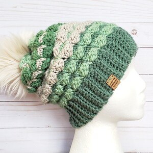 May include: A green, white and cream crocheted beanie with a fluffy white pom pom. The beanie has a brown leather tag that says "Kaitlynn's Crochet Glory".