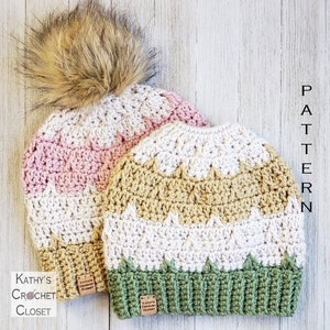 May include: Two crocheted hats, one with a pink, white, and brown color scheme and the other with a green, white, and brown color scheme. Both hats have a pom-pom on top and feature the text "Kathy's Crochet Closet".