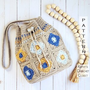 May include: A crocheted drawstring bag with a brown, blue, white, and yellow geometric pattern. The bag has a long strap and a tassel. The bag is on a white wooden surface. "PATTERN" is written vertically on the right side of the image. "Kathy's Crochet Closet" is written in the bottom right corner of the image.