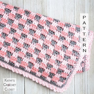 Puede incluir: Una manta de bebé de crochet rosa y gris con un borde festoneado. La manta está hecha con un patrón de punto simple y tiene un aspecto texturizado. El texto "PATTERN" es visible en la esquina superior derecha de la imagen.