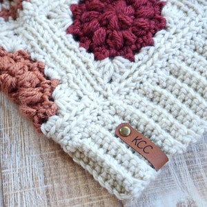 May include: A white crocheted hat with a brown leather label that says "KCC". The hat has a red and orange crocheted design.