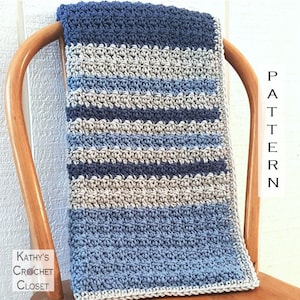 Puede incluir: Una manta de crochet a rayas azules y grises drapeada sobre una silla de madera. La manta tiene un patrón de puntada texturizado y está hecha con hilo suave. El texto "PATTERN" es visible en el lado derecho de la imagen.